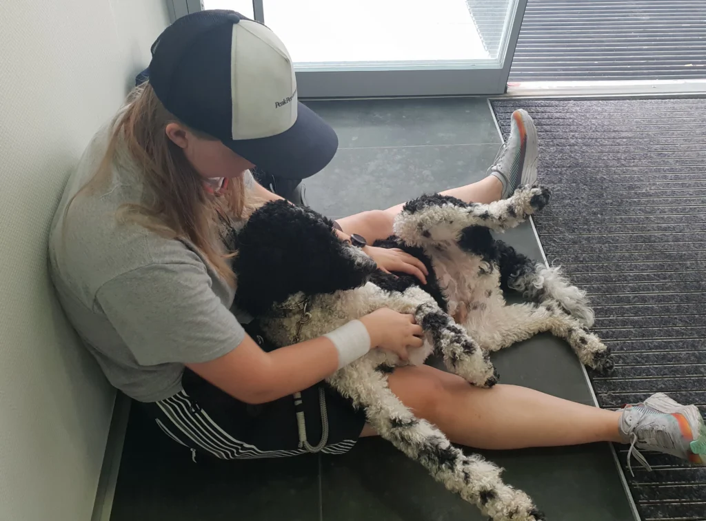 Frau sitzt am Boden. Ein Hund liegt zwischen ihren Beinen.