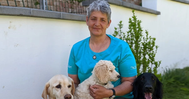 Lächelnde Frau mit Welpen am Schoß und zwei Hunden neben ihr.