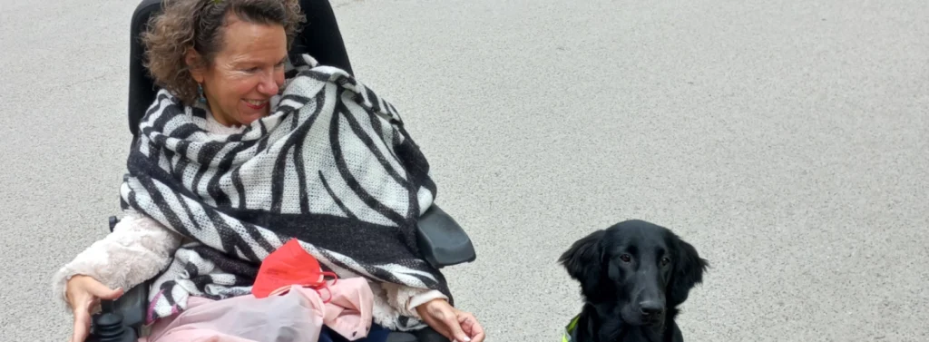 Eine Frau im Rollstuhl lächelt den Hund neben ihr an.