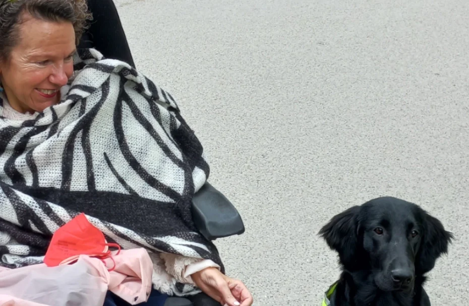 Eine Frau im Rollstuhl lächelt den Hund neben ihr an.