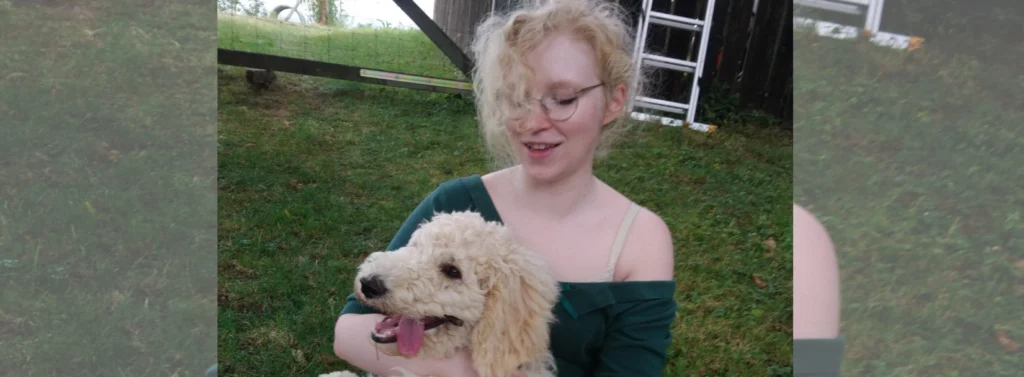 Frau sitzt mit Hund auf ihrem Schoß auf einer Wiese.