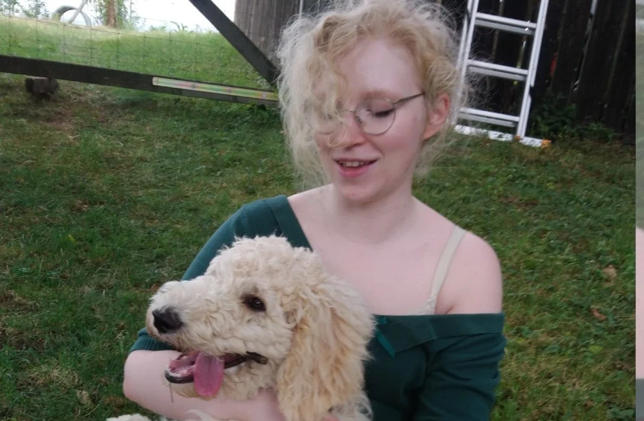 Frau sitzt mit Hund auf ihrem Schoß auf einer Wiese.