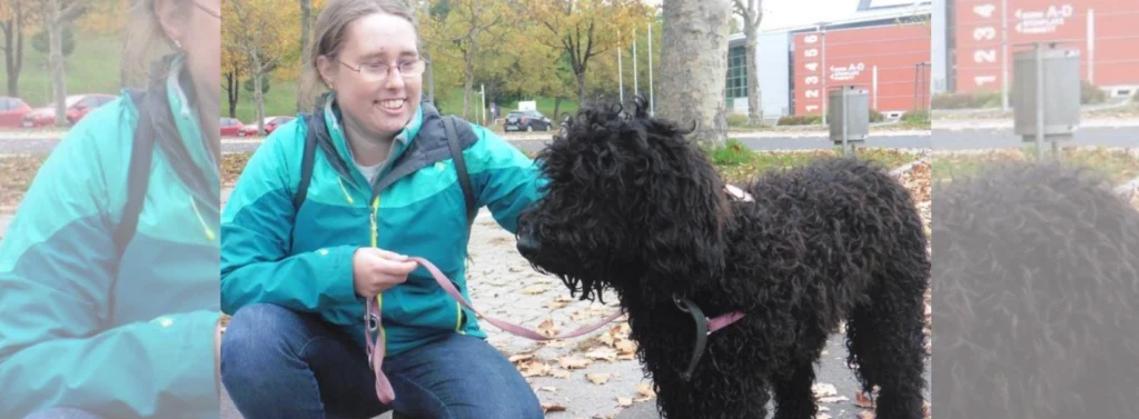 Lächelnde Frau kniet am Boden und streichelt Hund.