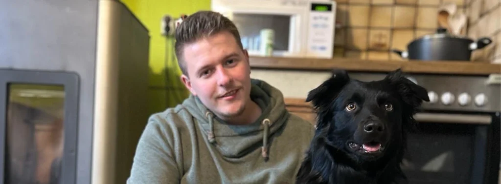 Mann sitzt auf Küchenboden und umarmt einen Hund.