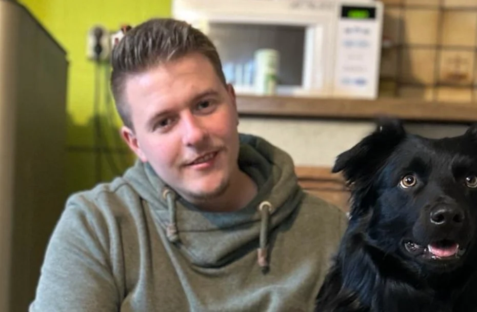 Mann sitzt auf Küchenboden und umarmt einen Hund.