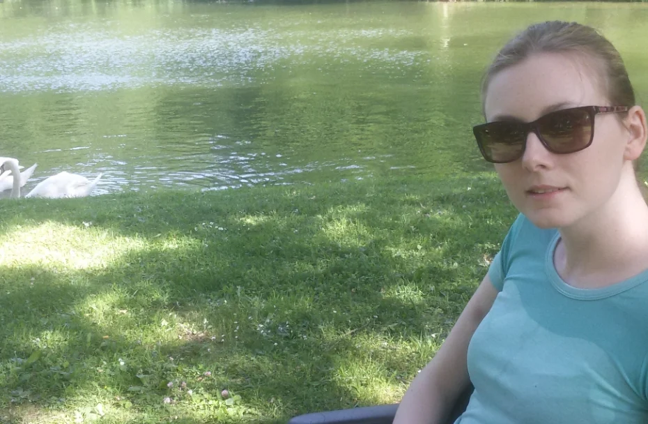 Frau sitzt in Wiese vor See.
