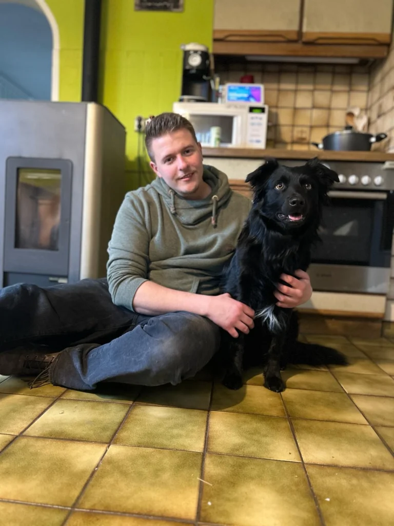 Mann sitzt auf Küchenboden und umarmt einen Hund.
