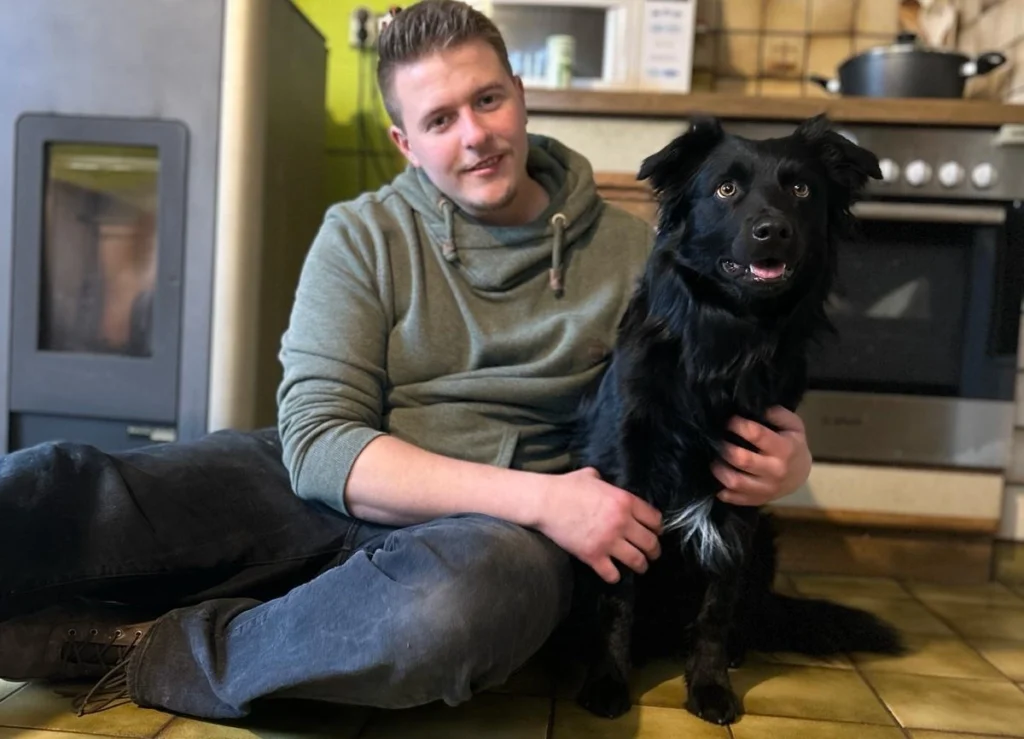 Mann sitzt am Boden und umarmt Hund.