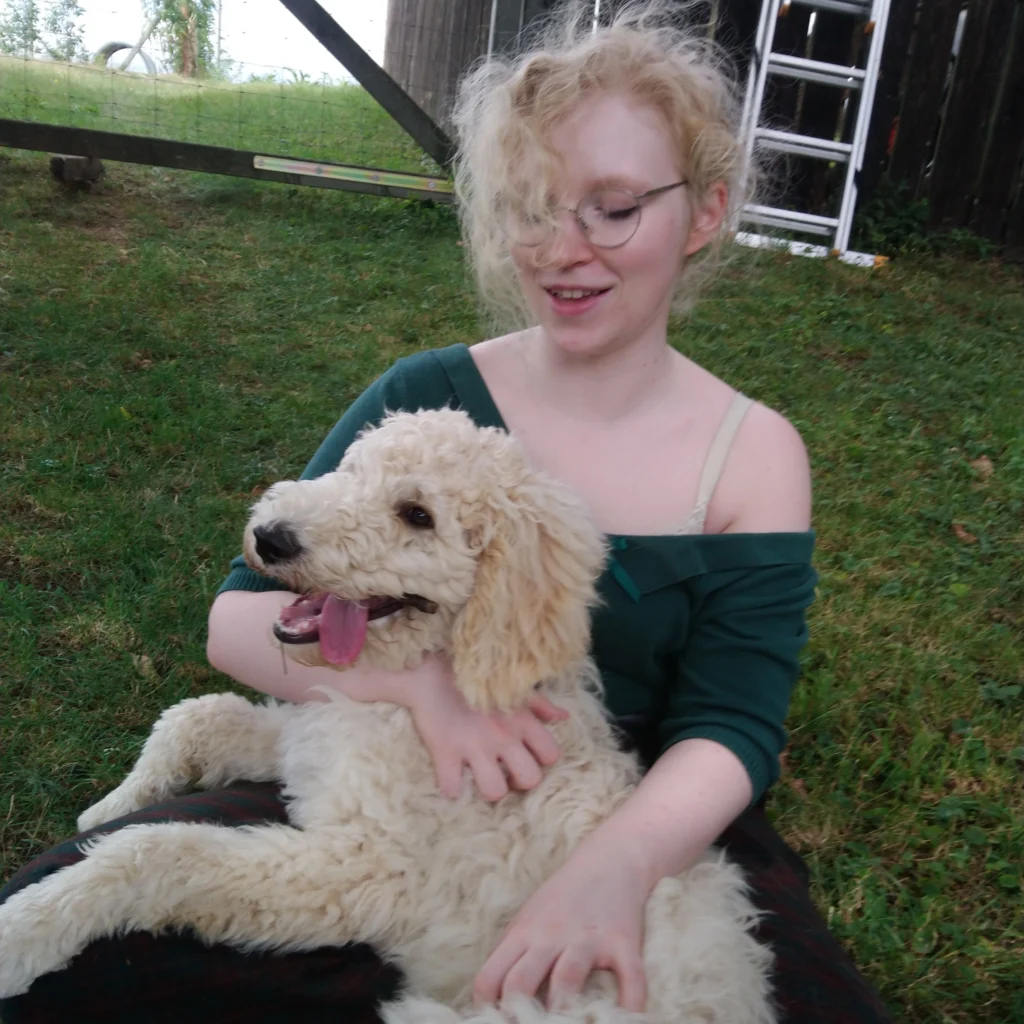 Frau sitzt mit Hund auf ihrem Schoß auf einer Wiese.