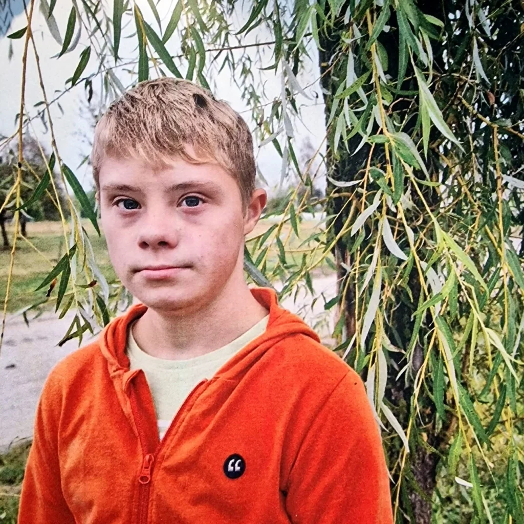 Junge steht vor Baum.