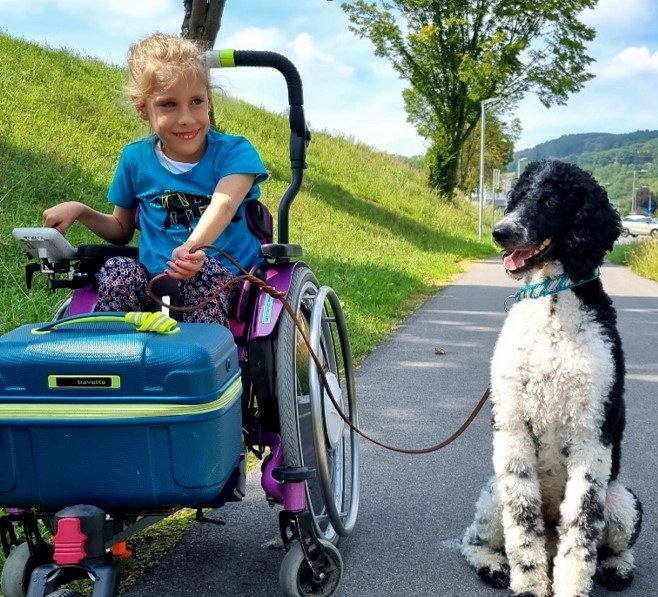 Mädchen im Rollstuhl hält Hund an der Leine.