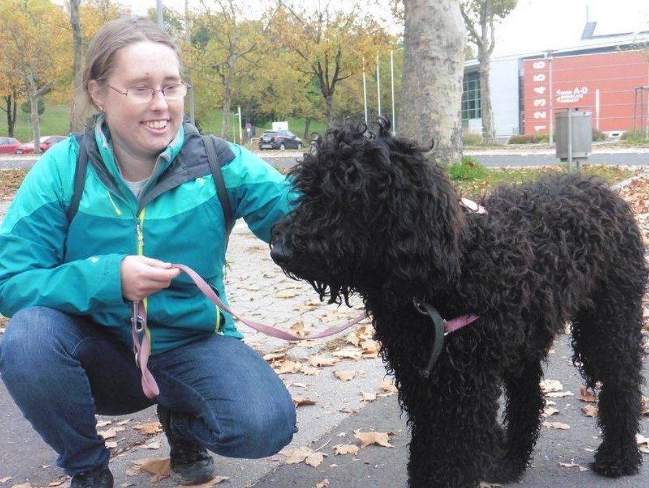 Lächelnde Frau kniet am Boden und streichelt Hund.