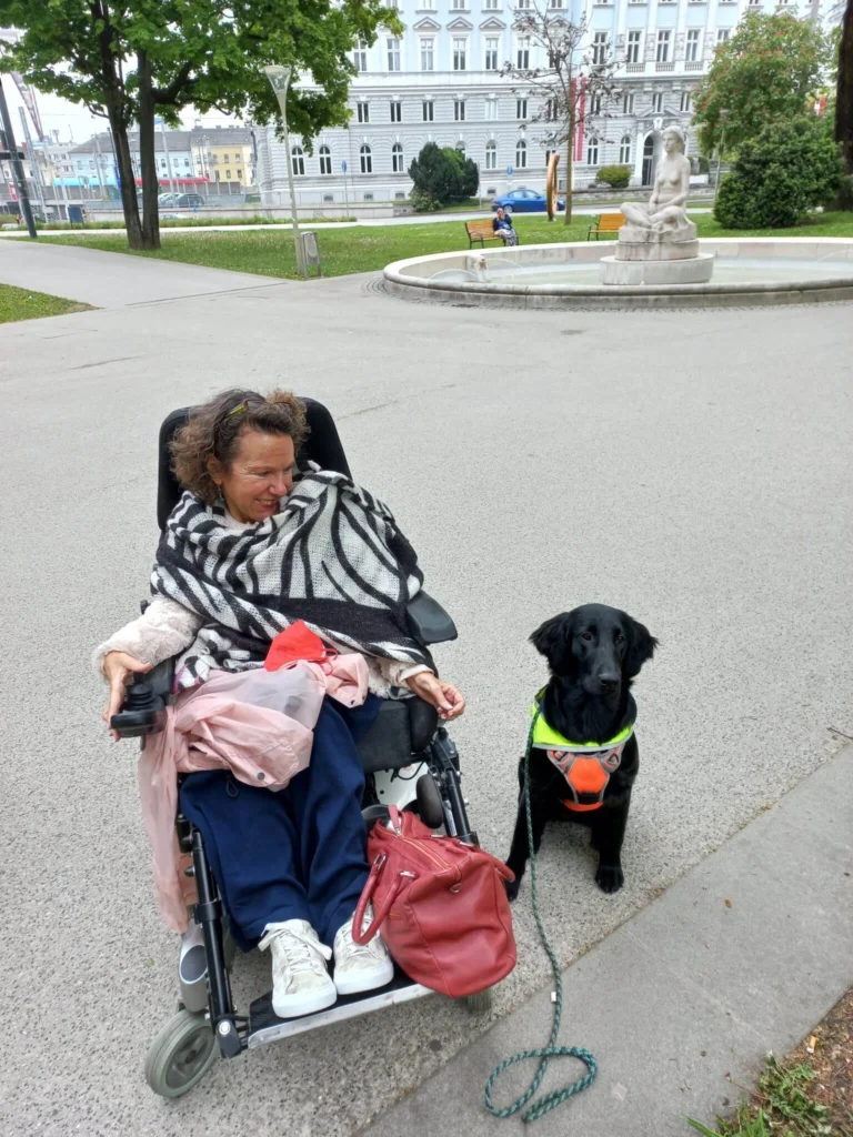 Eine Frau im Rollstuhl lächelt den Hund neben ihr an.